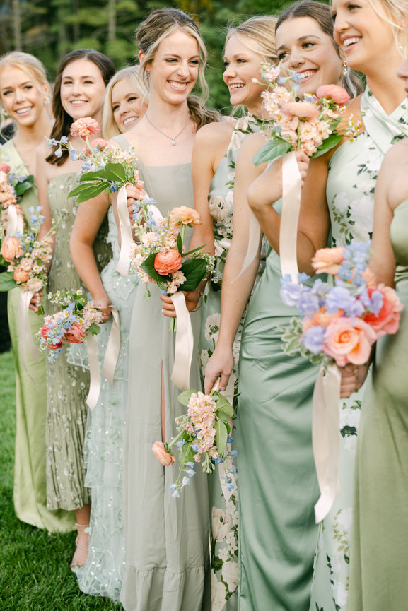Bridesmaids in varied solid and printed green dresses holding varied and colorful bouquets. Wedding photography by Heather Durham.