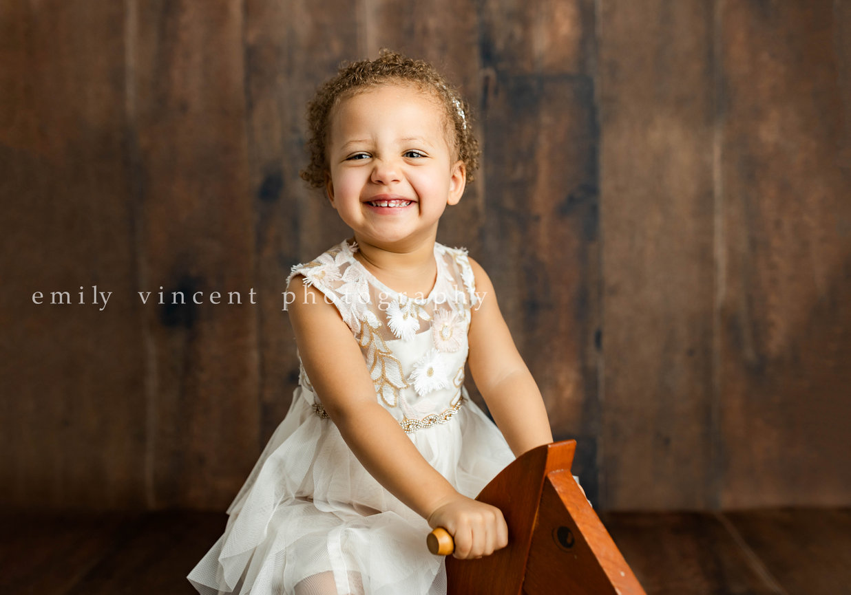 Close-up on young girl smiling while holding onto rocking wooden horse