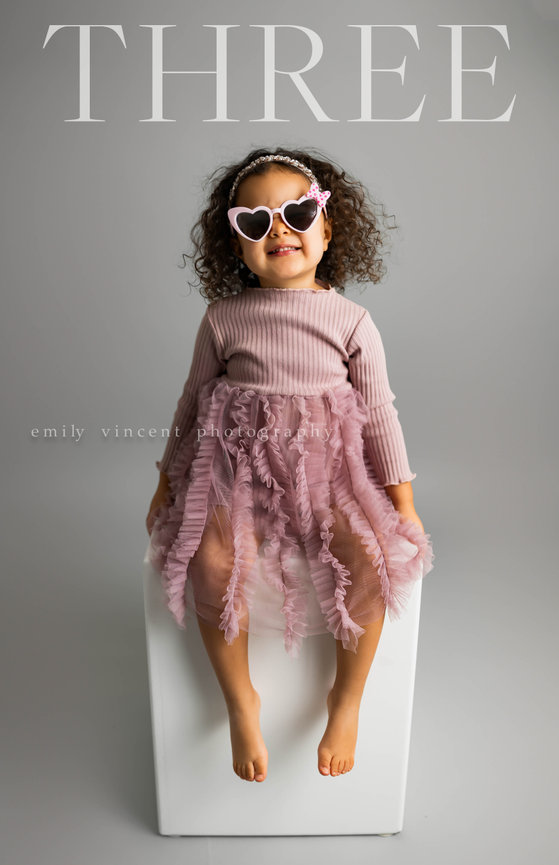 Girl wearing tulle dress posing in neutral background with THREE across the top