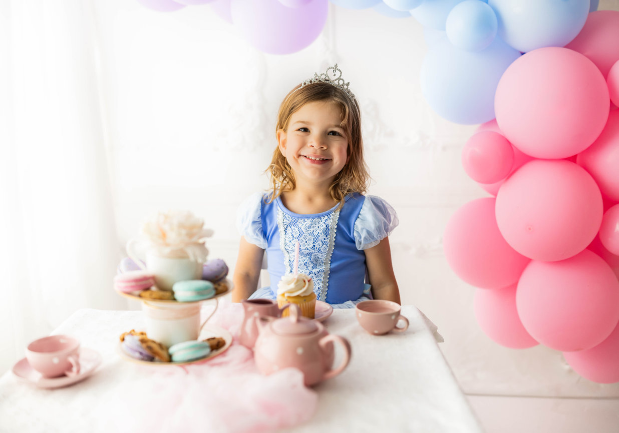 Young child smiling in front of tea party props with balloons and crown