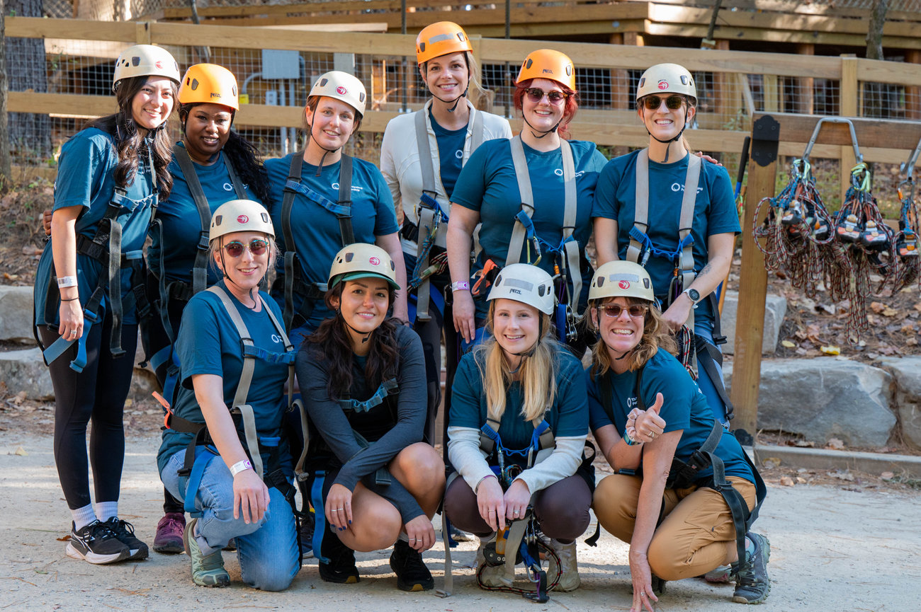 A group of eleven people in helmets and harnesses posing together in an outdoor adventure setting captured in the style of Jo Hayes Images Charlotte Event Photography The Whitewater Center company outing