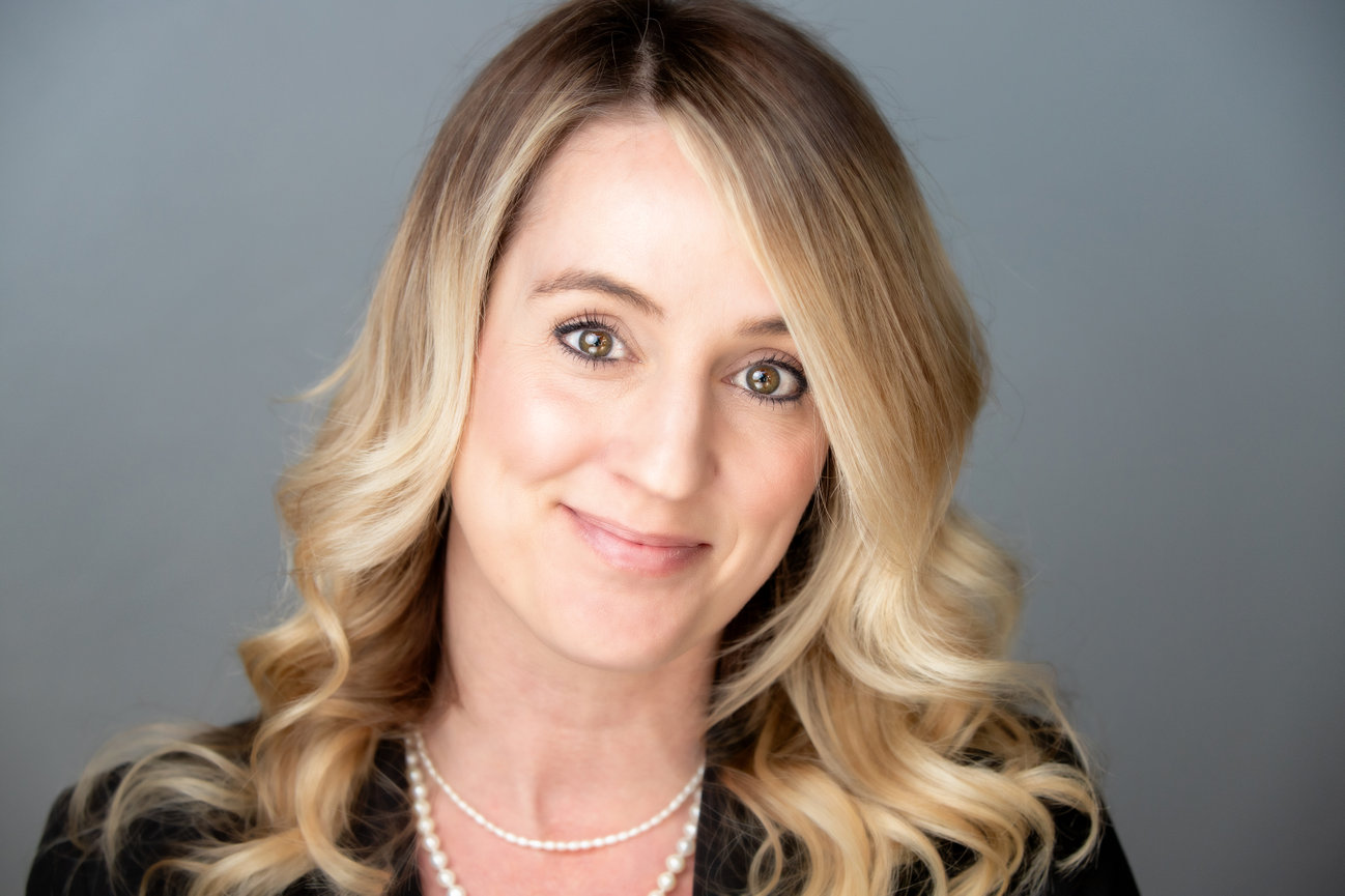 Smiling blonde woman in a studio portrait with gray background and pearl neckla