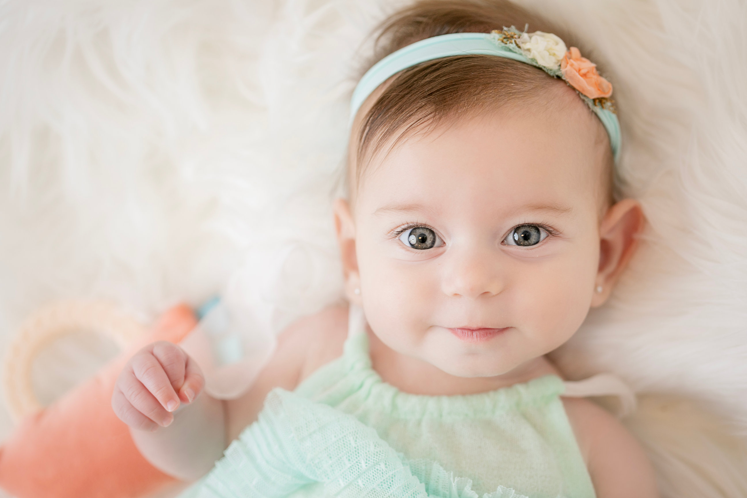 Baby lifting one hand in a mint green dress
