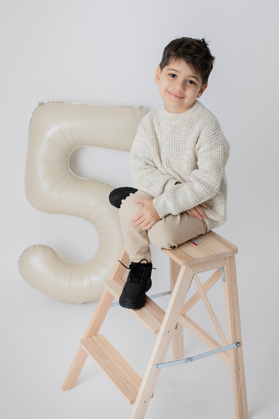 A child seated beside a large number-five balloon for a birthday portrait.