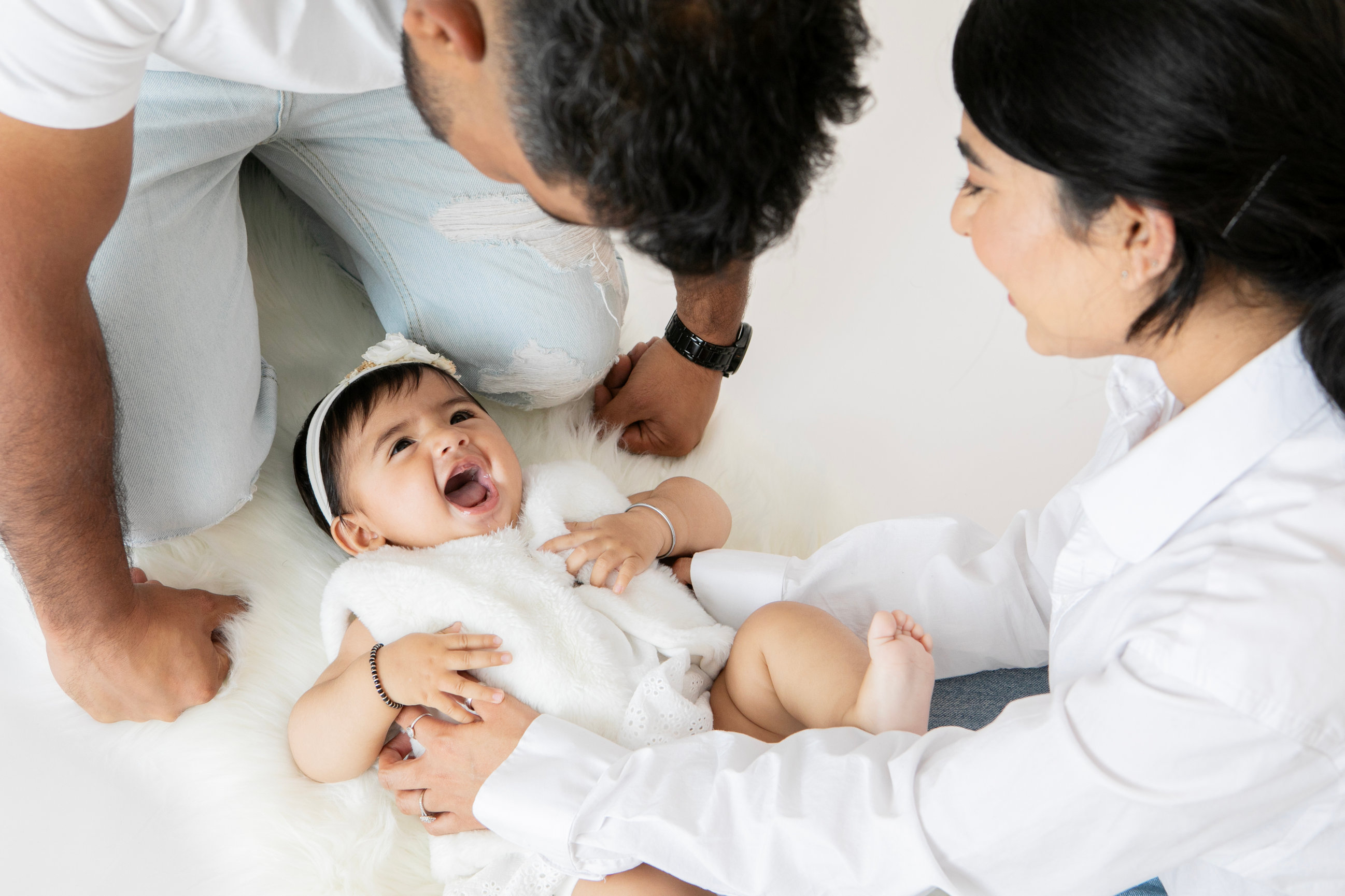 Parents leaning close to their baby on a soft white blanket