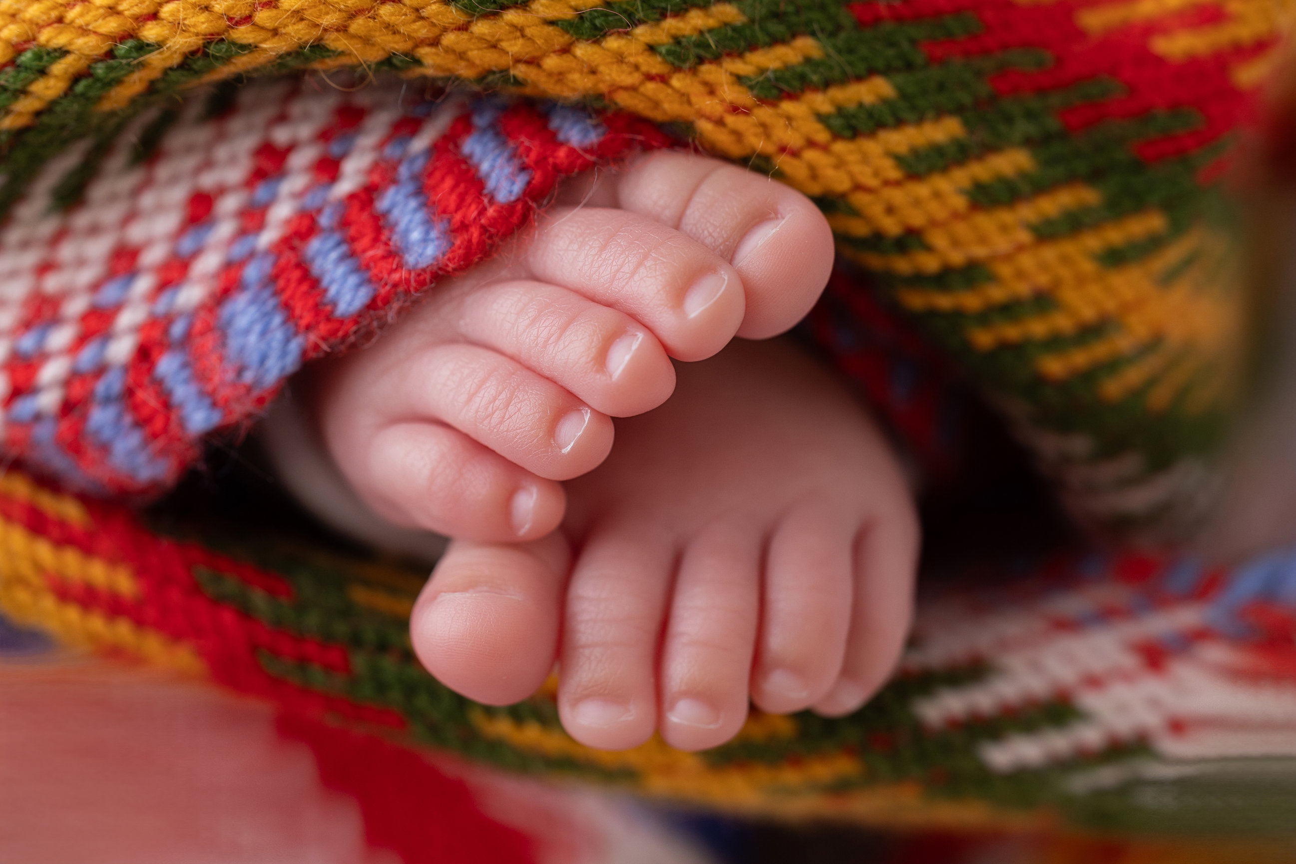 Close-up of a newborn girl’s toes against the woven arrow pattern of a Métis sash