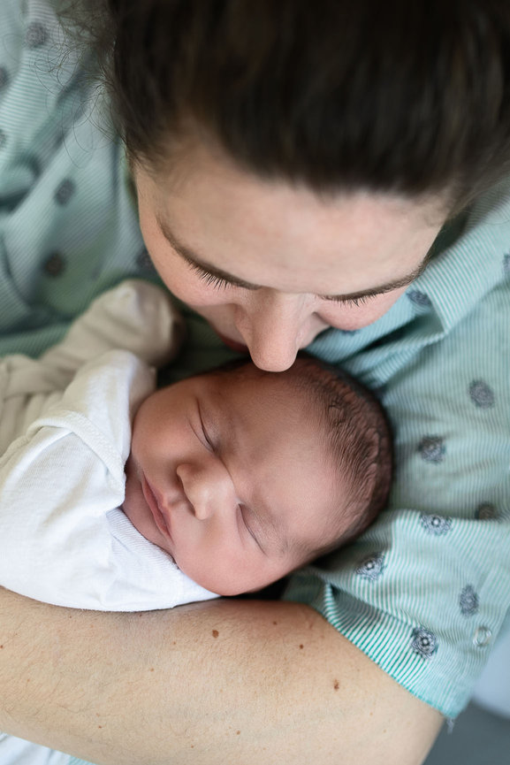 A woman lovingly holds a sleeping newborn baby in her arms at Northwestern Medicine Huntley Hospital. The baby, wrapped in a white blanket, peacefully rests as the mother gently leans in, showing an expression of tenderness and care.
