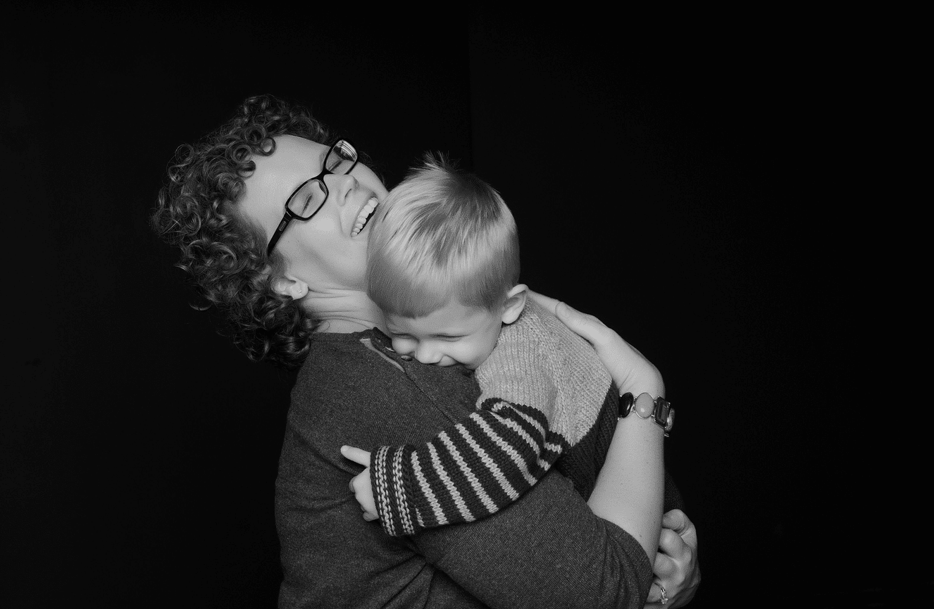 A mother laughing as she warmly embraces her toddler son.