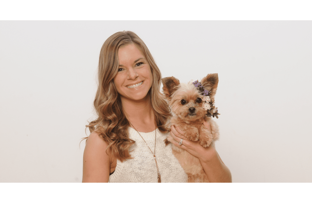 A small blonde furry puppy with a floral wreath hanging off her ear with her owner Emily in the Kliks Photography studio in Cedar Rapids Iowa.