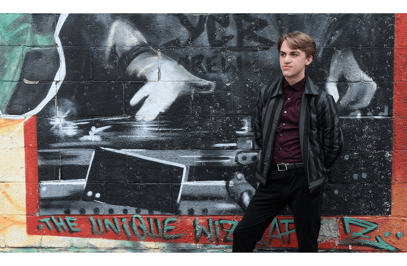A high school musician stands in front of a wall of graffiti.