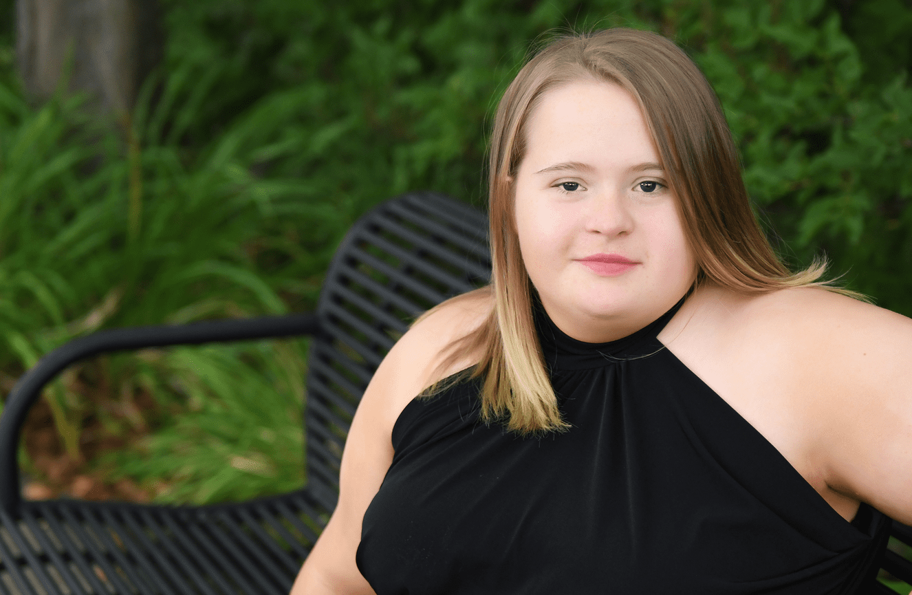 A young woman in a black cocktail dress sitting on a park bench.