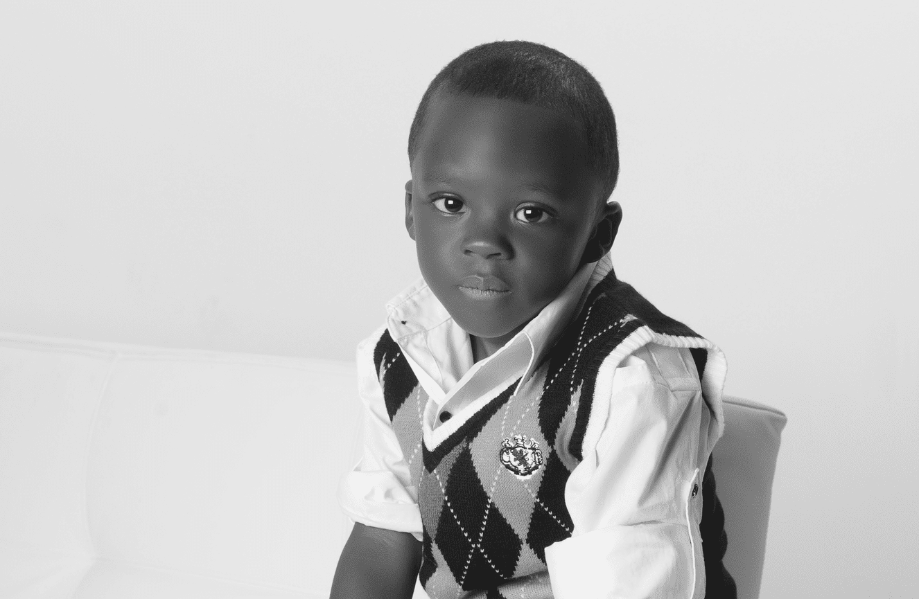 A young African-American boy in a sweater vest looks quietly into the camera.