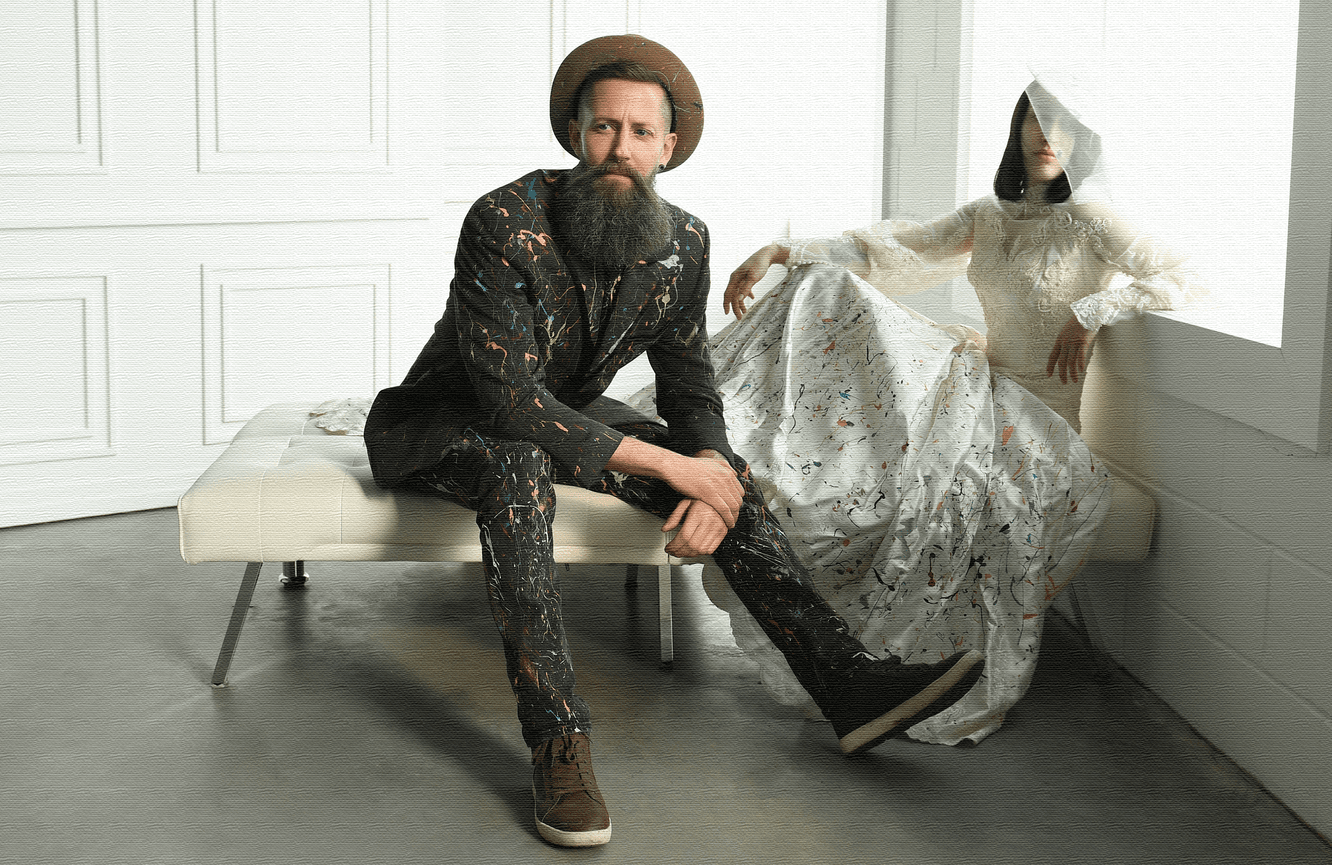 A man in a painted suit and a woman in an artful wedding dress sit on a couch looking contemplative in the Kliks Photography studio in Cedar Rapids, Iowa.