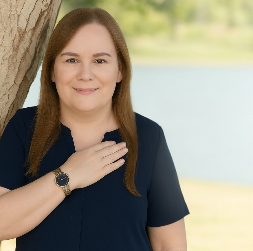 Portrait of Sherry Dansby, a transgender woman with blondish-red hair, smiling in a royal blue blouse against a soft lake background.