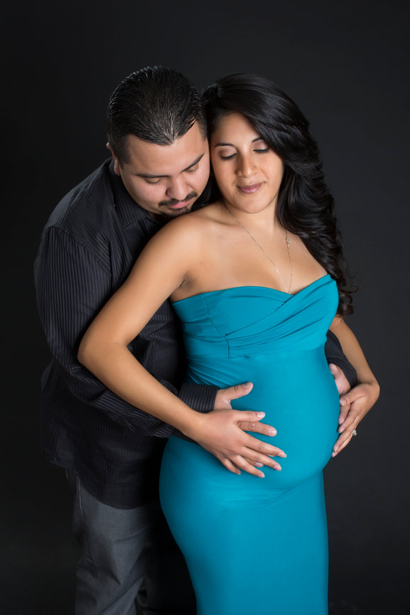 Expecting couple posed together in a romantic maternity portrait.  Their eyes are closed and both their hands are resting together on the woman's belly as they are embracing.
