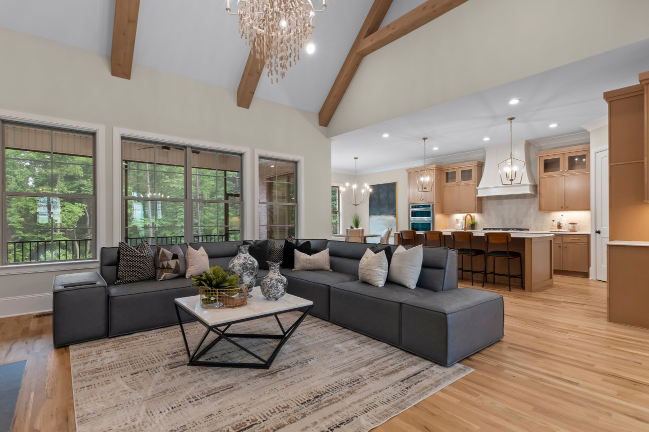 Modern open-concept living room and kitchen with large windows, vaulted ceiling, and gray sectional sofa