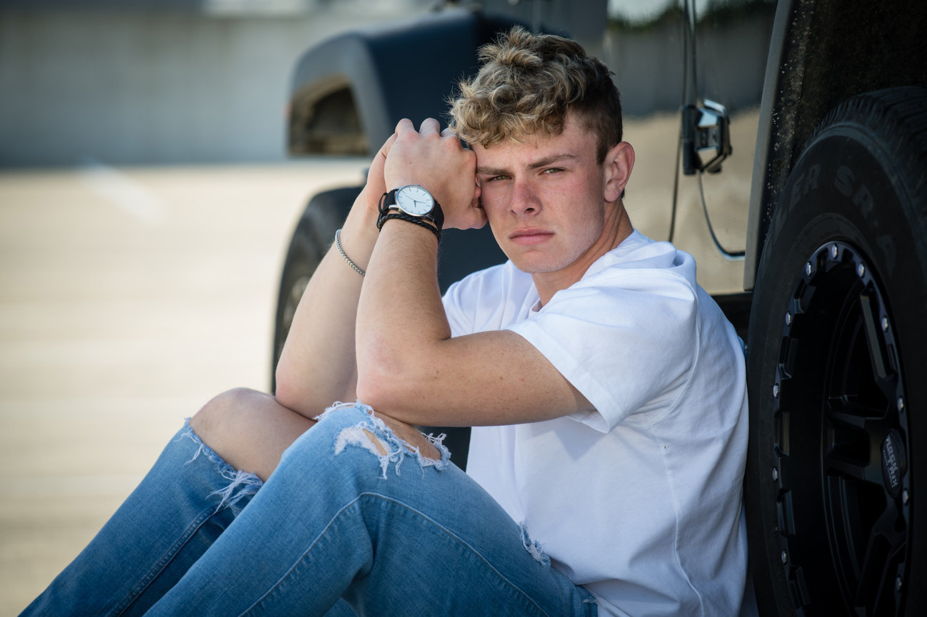 Teenage blond boy in a white tee and ripped jeans leaning against a jeep for senior pictures in Columbus OH.