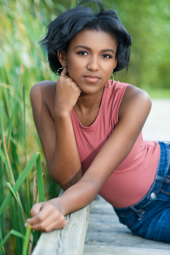 Beautiful teen girl sitting on a wooden boardwalk surrounded by tall grasses in a rustic park setting