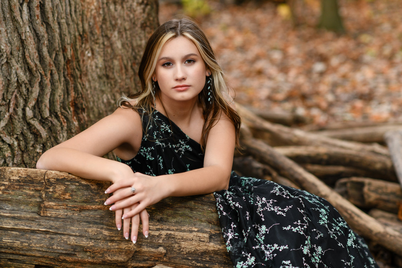 Teenage girl in a black and white floral dress sitting on a log for senior photos in Columbus OH.