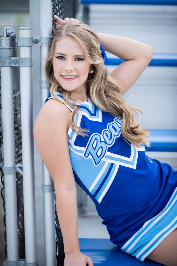 Cheerleader in a blue uniform posing on bleachers with a confident smile.