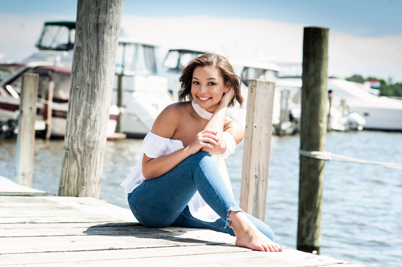 Teenage girl sitting on a dock in jeans and a white blouse for senior pictures in Dublin OH.