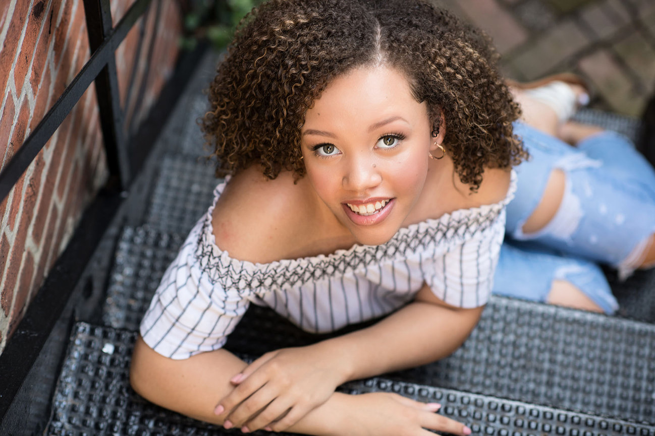 teen girl sitting on stairs being photographed from above with an off the shoulder shirt and jeans for her senior pictures in Columbus Ohio
