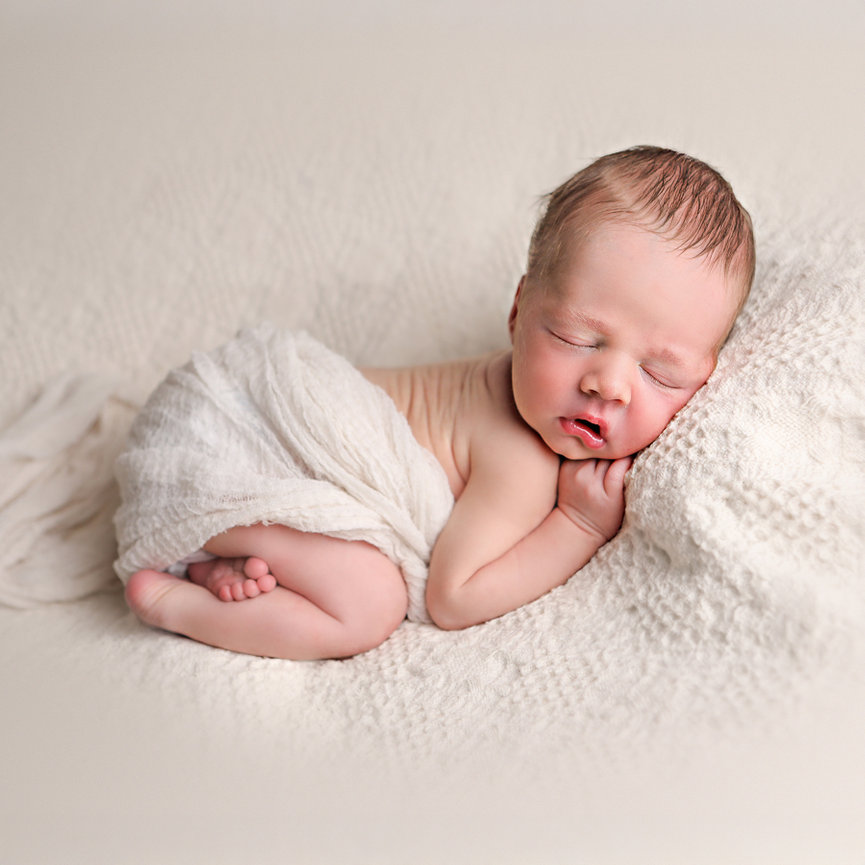 Newborn baby sleeping peacefully on a soft, white blanket.