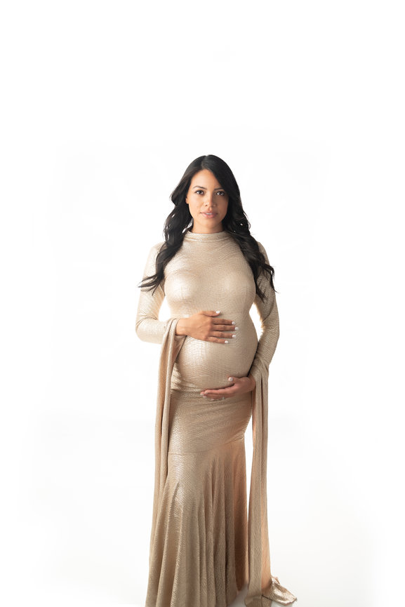Timeless pregnancy portrait of expectant mother in a minimalist studio, wearing a luxury gold gown.